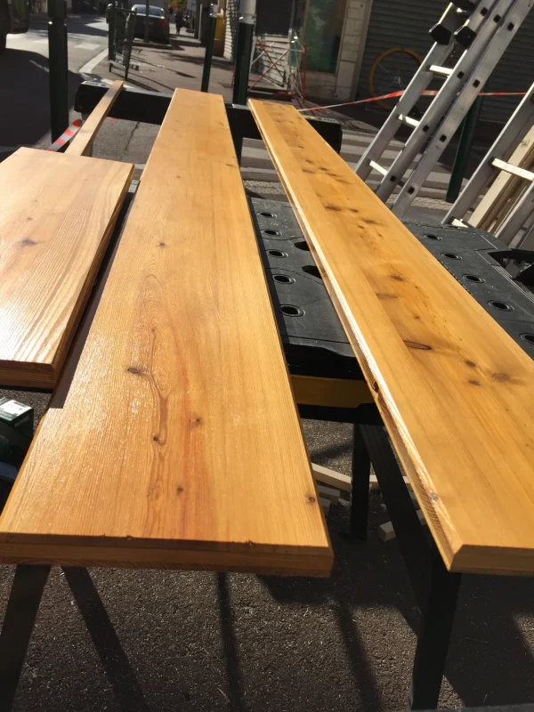 Planches de bois brut posées sur tréteaux, préparation d'une enseigne sur le trottoir.