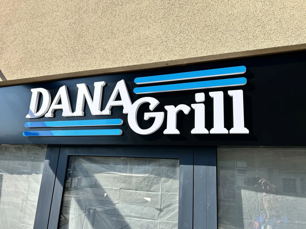 Bandeau noir DANA Grill avec lettres blanches en relief et filets bleus au-dessus d'une vitrine.