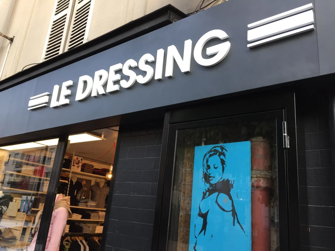 Enseigne « Le Dressing » en lettres blanches en relief sur bandeau noir, devanture de boutique de vêtements.
