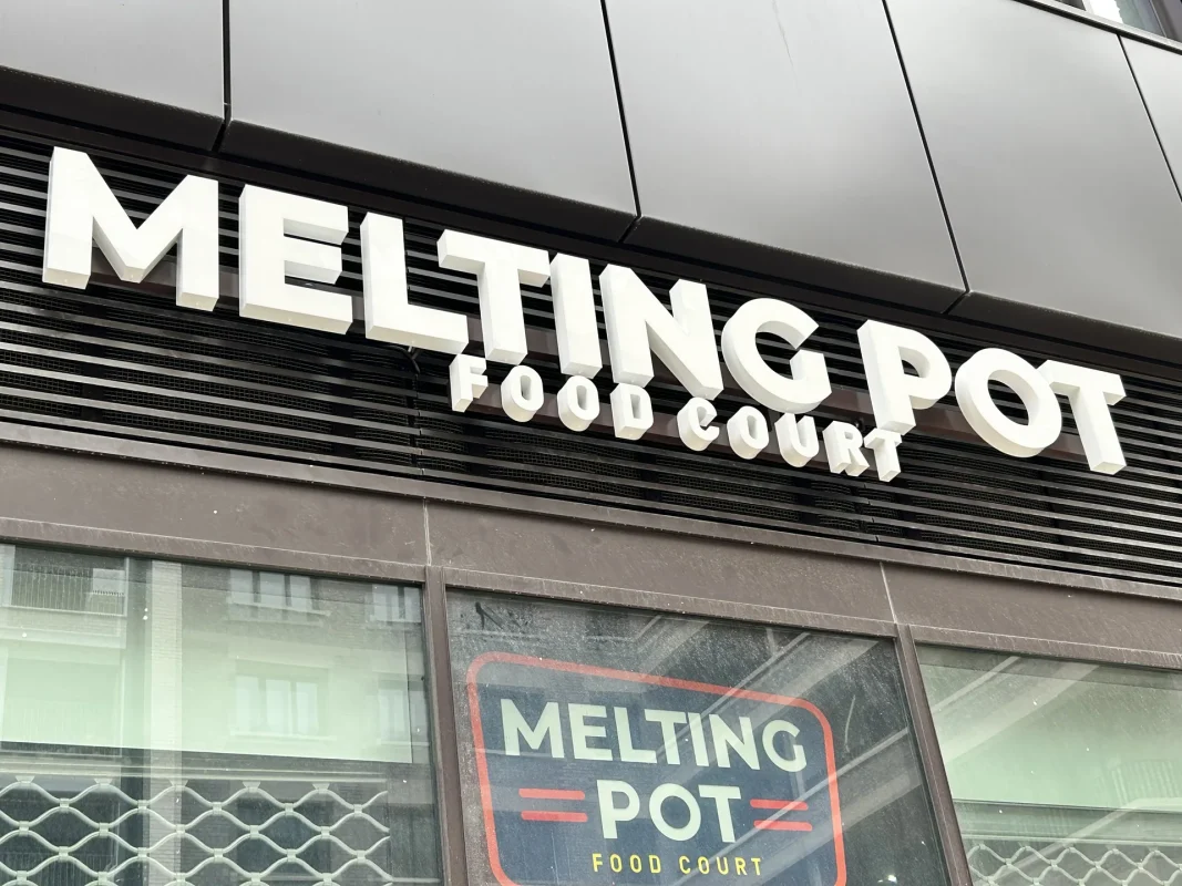 Lettres blanches en relief de l'enseigne Melting Pot au-dessus d'une vitrine, avec le logo Food Court.