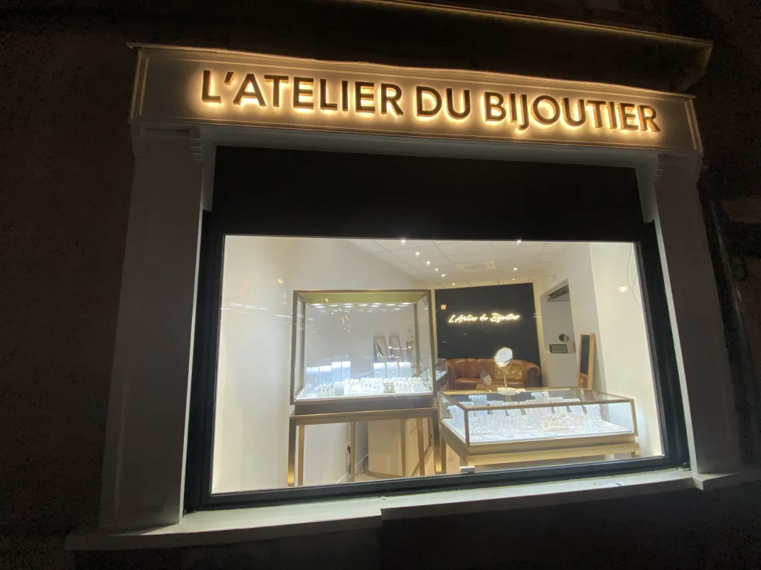 Vitrine de nuit de L'Atelier du Bijoutier, avec son enseigne lumineuse en lettres relief.