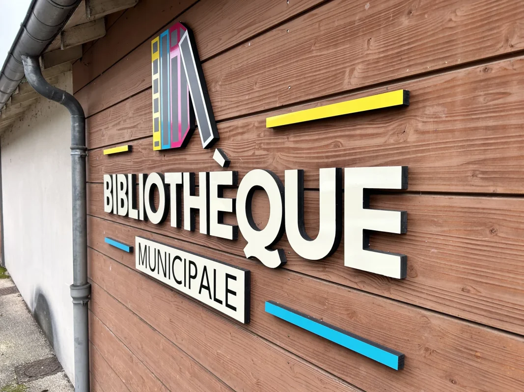 Enseigne BIBLIOTHÈQUE MUNICIPALE en lettres relief colorées sur un bardage en bois.
