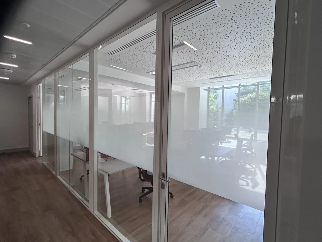 Cloisons vitrées de bureaux partiellement habillées d'un film dépoli, le long d'un couloir clair.