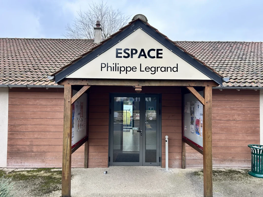 Fronton ESPACE Philippe Legrand au-dessus de l'entrée d'un bâtiment en bois, avec porte vitrée.