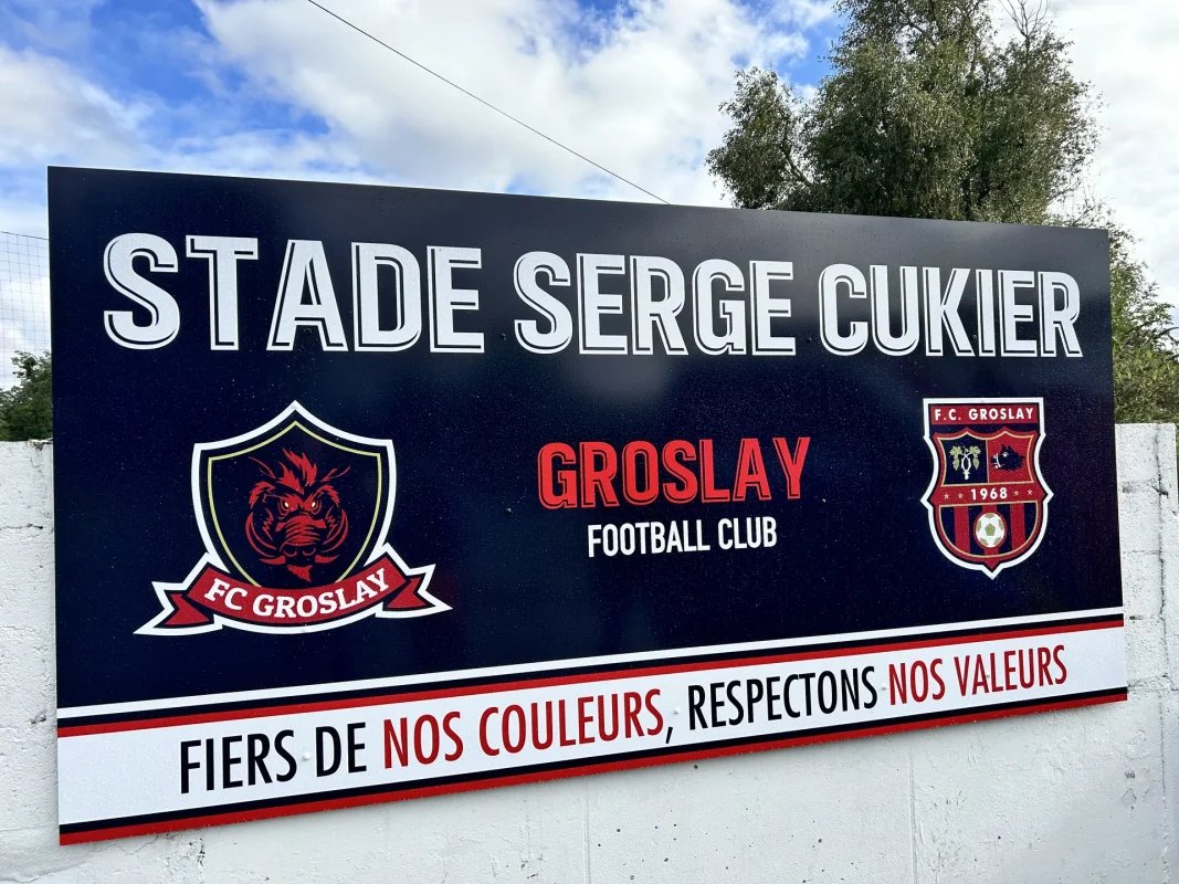 Panneau du FC Groslay vu de biais, avec l'écusson du club et la devise sous le logo.
