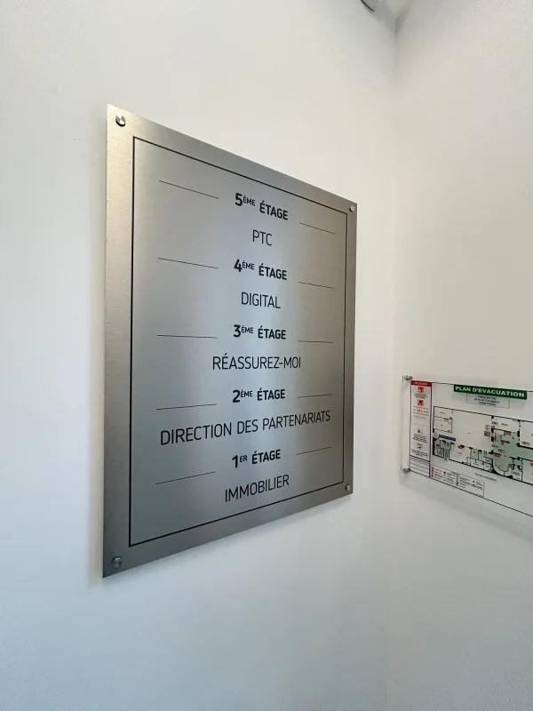 Plaque inox gravée listant les étages d'un immeuble de bureaux, plan d'évacuation à droite.