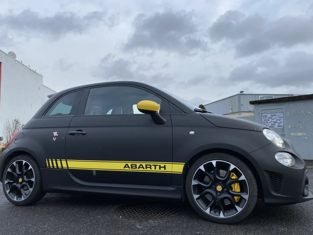 Petite sportive noir mat en extérieur, bande jaune sur le flanc.
