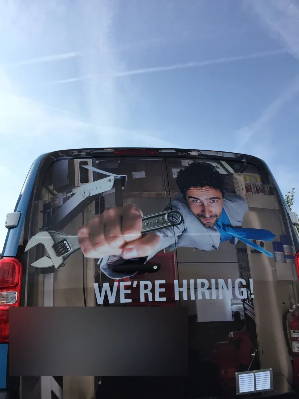 Arrière de fourgon avec l'inscription We're hiring et un mécanicien tenant une clé anglaise.
