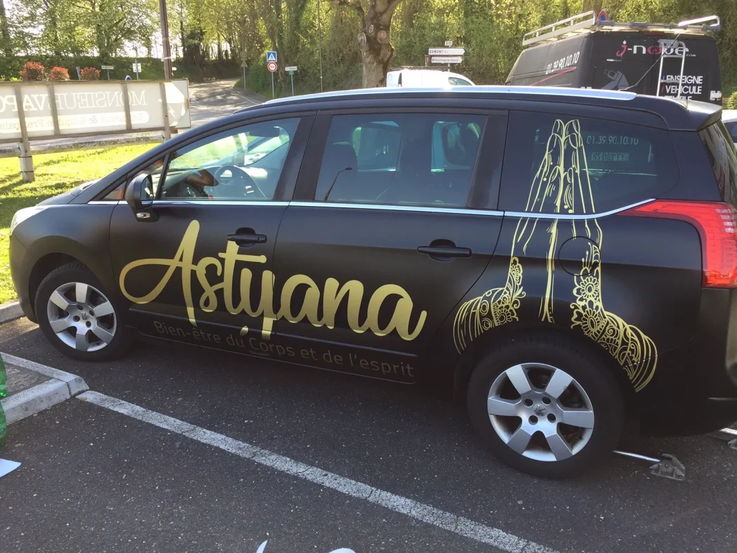 Monospace noir mat avec décor doré Astyana, vu de côté sur un parking.