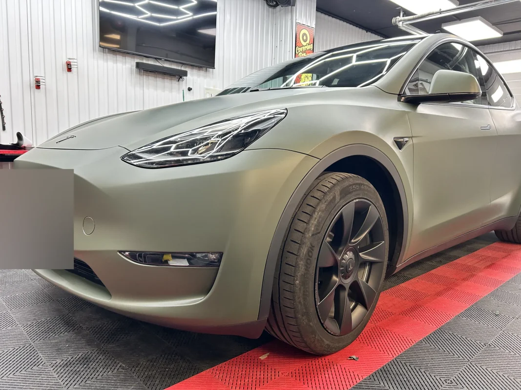 SUV électrique habillé d'un covering vert kaki mat, en atelier, vue de trois quarts avant.